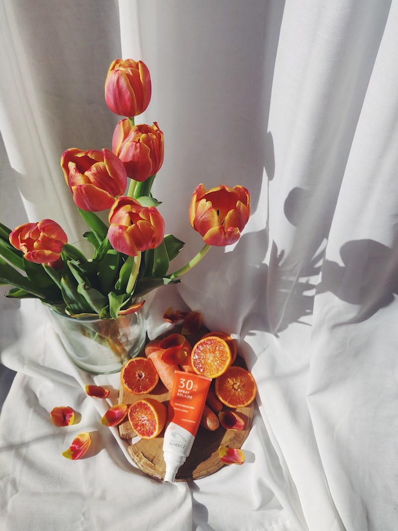 Stillborn. White curtain, orange tulips, carrots, oranges and Alga Maris sunscreen